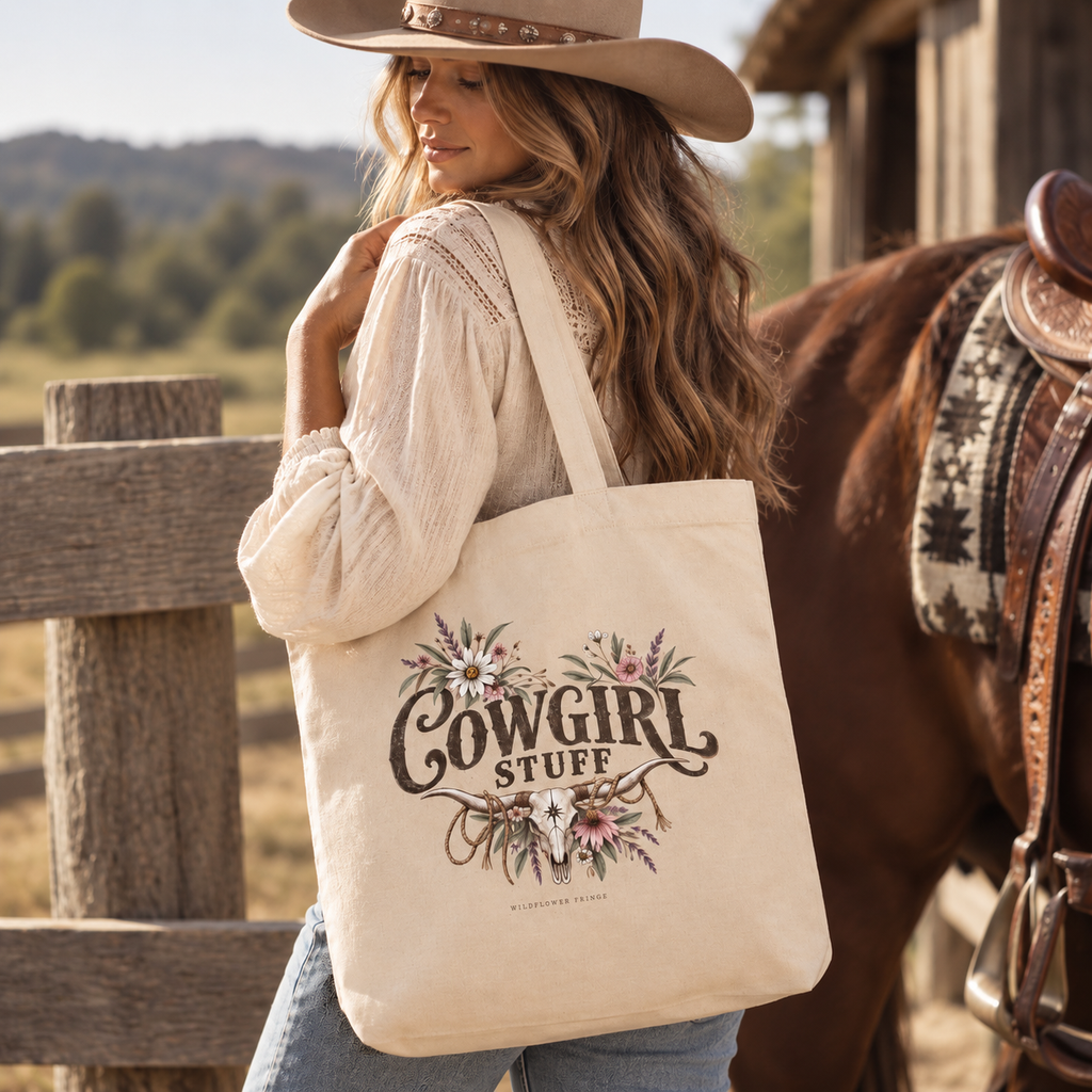 A woman in a cowboy hat and cream blouse carries a large cream canvas tote bag printed with 'Cowgirl Stuff' and floral artwork, standing beside a brown horse in a rustic outdoor setting.