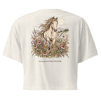 An off-white short-sleeve crop top shown from the back, featuring a large graphic of a white horse running through colorful wildflowers under a full moon, with the text 'WILDFLOWER FRINGE' printed below.