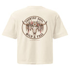 An off-white short-sleeve t-shirt showing the back graphic, which features a circular design with a longhorn skull decorated with flowers and feathers, surrounded by the text 'COUNTRY SOUL WILD & FREE'.